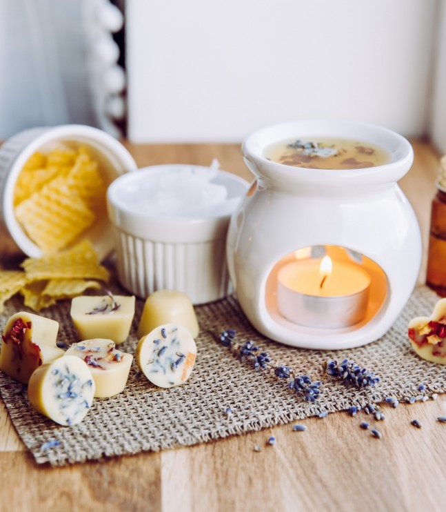 Using homemade mini wax melts in aromatherapy lamp diffuser at home interior concept. Melts making ingredients on table for unbleached beeswax, solid coconut oil, essential oil, dried flowers.